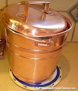 Shiny copper bucket with a lid on a countertop.